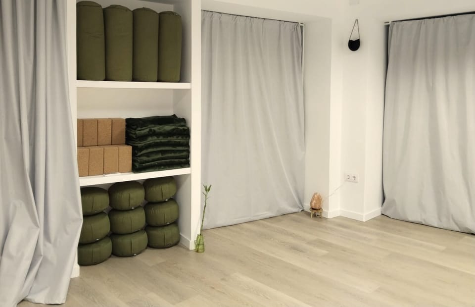 Estantería del centro con bolsters verdes, bloques de corcho, mantas y cojines de meditación.