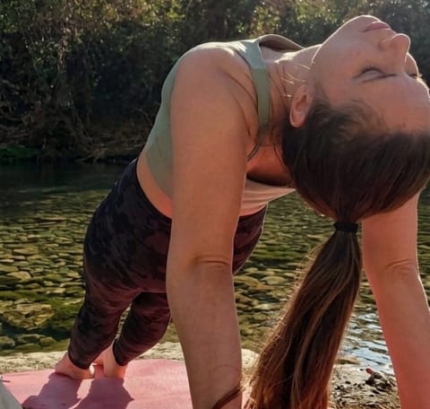 Mujer haciendo una extensión de espalda al aire libre junto al río, a la luz del atardecer.